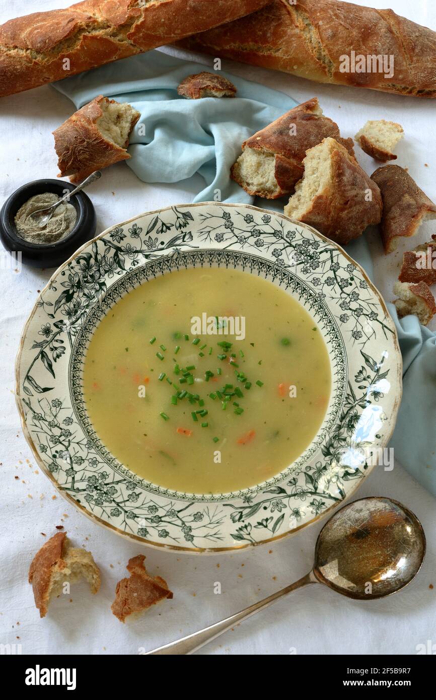 Crème de soupe de légumes avec garniture de ciboulette dans l'antique victorien bol à soupe avec cuillère à soupe vintage et morceaux de baguettes fraîchement cuites Banque D'Images