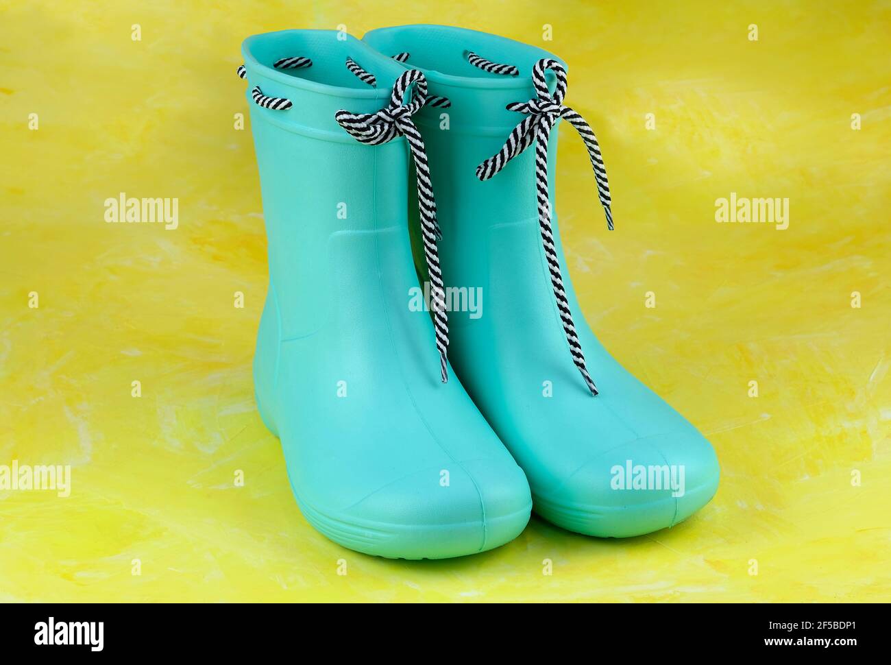 Bottes en caoutchouc vert sur fond jaune. Chaussures pour temps pluvieux. Bottes en caoutchouc pour femmes avec cordon. Banque D'Images