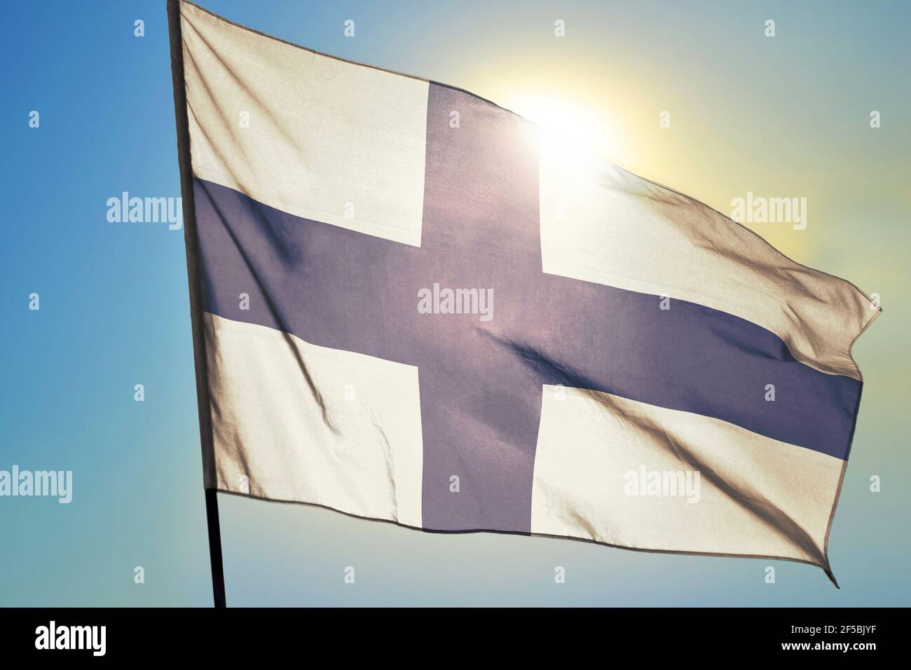 Drapeau finlandais agitant sur le vent devant le soleil Banque D'Images