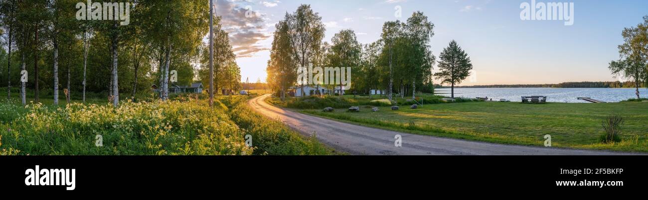 Panorama pittoresque de la forêt de bouleau suédois, village d'été, lac et magnifique lumière de coucher de soleil sur la route de campagne. Suède. Banque D'Images