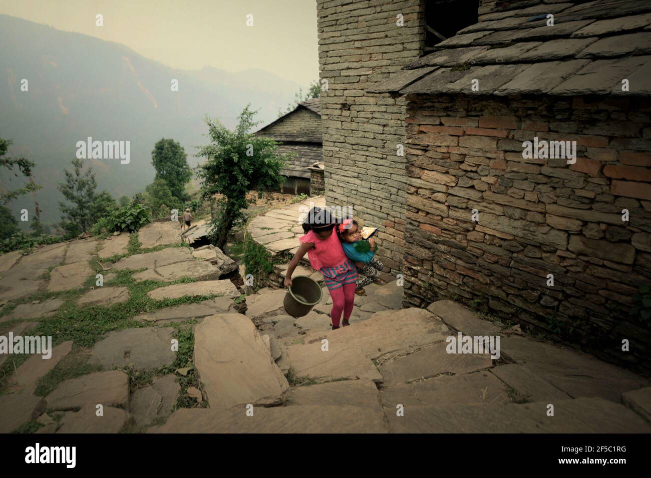Un enfant portant sa petite sœur tout en faisant des marches lapidées, alors qu'ils vont prendre de l'eau dans une installation commune d'eau dans le village de Damdame dans la région de Panchase, Gandaki Pradesh, Népal. En 2017, environ 4.2 milliards de personnes, soit 55 % de la population mondiale, n'avaient pas accès à des services d'assainissement gérés en toute sécurité, selon ONU Water dans leur Résumé Progress Update 2021, publié le 1er mars 2021 à Genève. Banque D'Images