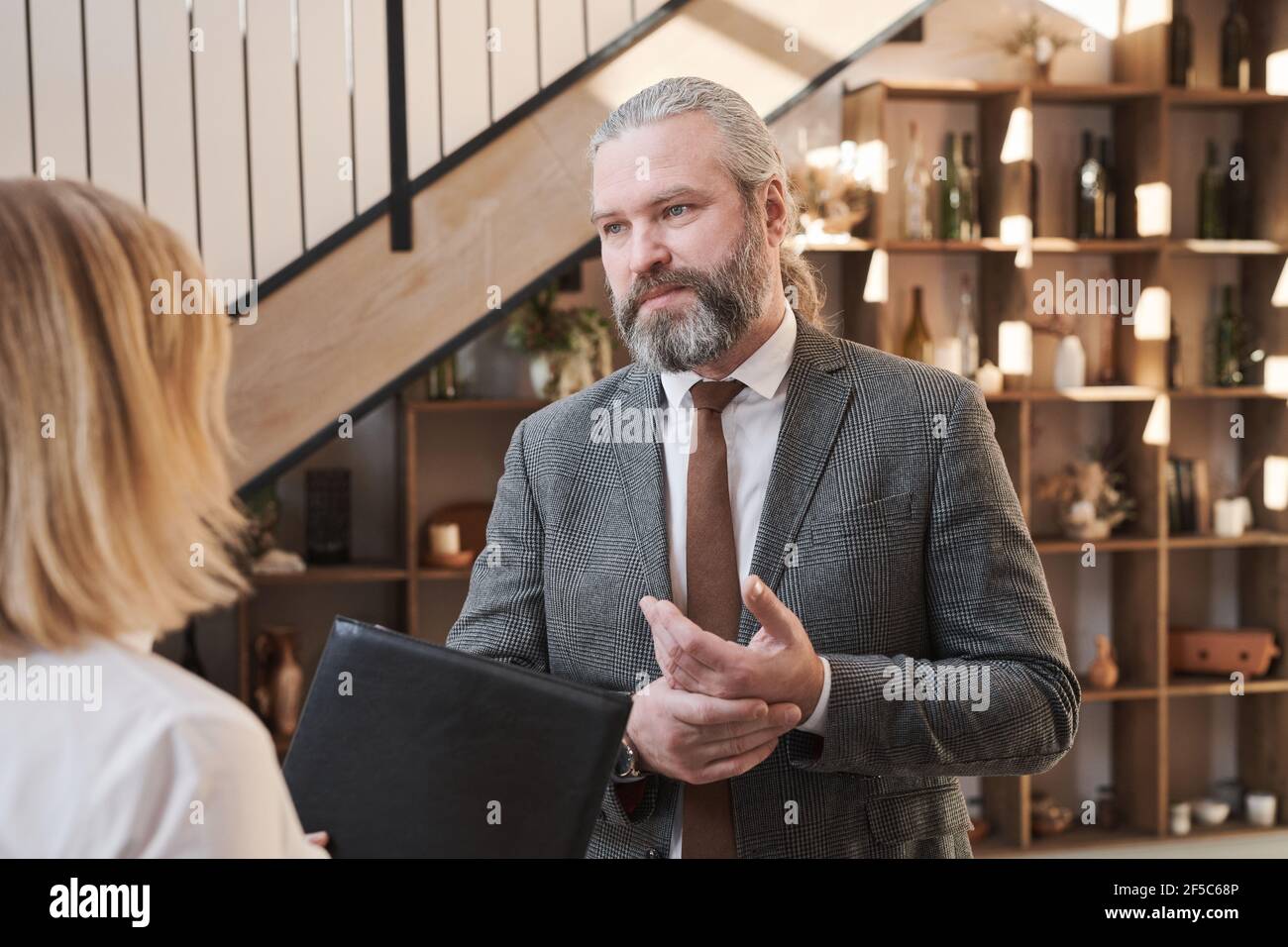 Homme d'affaires mûr et barbu parlant à l'employé pendant qu'il se tient debout bureau Banque D'Images