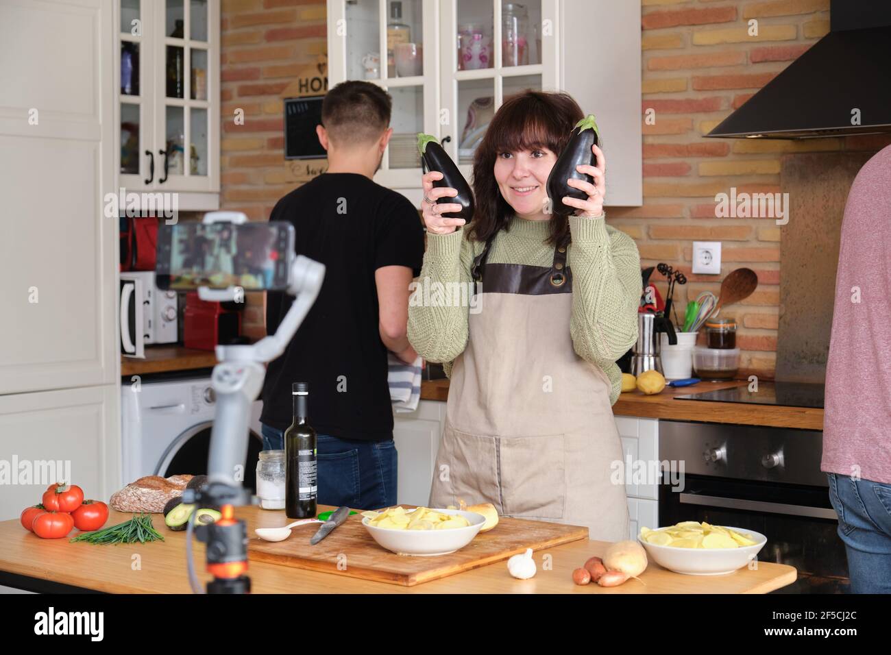 Jeune femme montrant deux aubergines à la caméra pendant qu'elle enregistre une vidéo avec son smartphone pour sa chaîne de cuisine. Créateur de contenu et influenceur Banque D'Images
