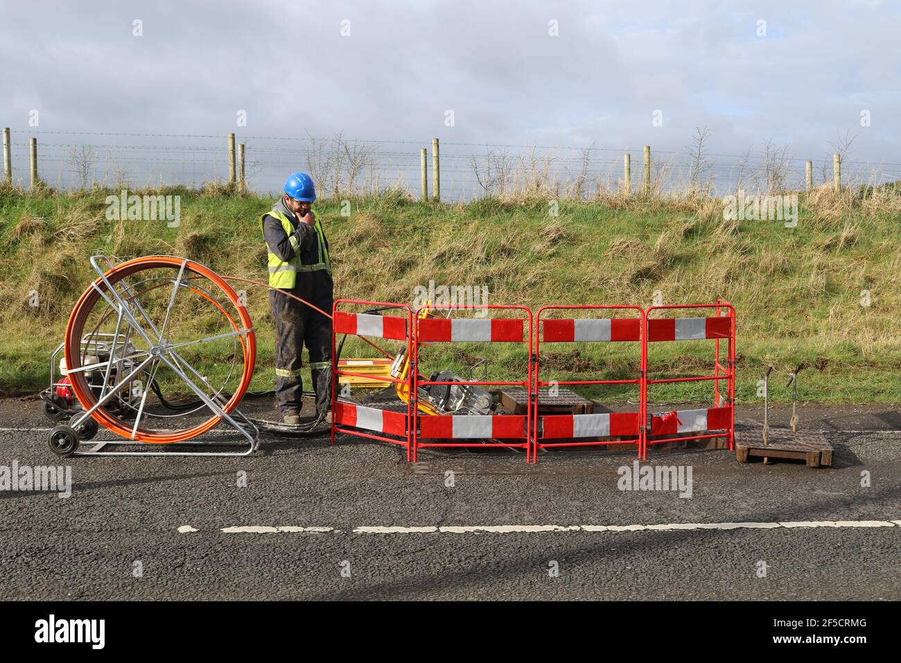 Un homme regarde dans un trou en installant des câbles à fibres optiques sur une route rurale à l'extérieur de Lisburn, en Irlande du Nord, au Royaume-Uni Banque D'Images