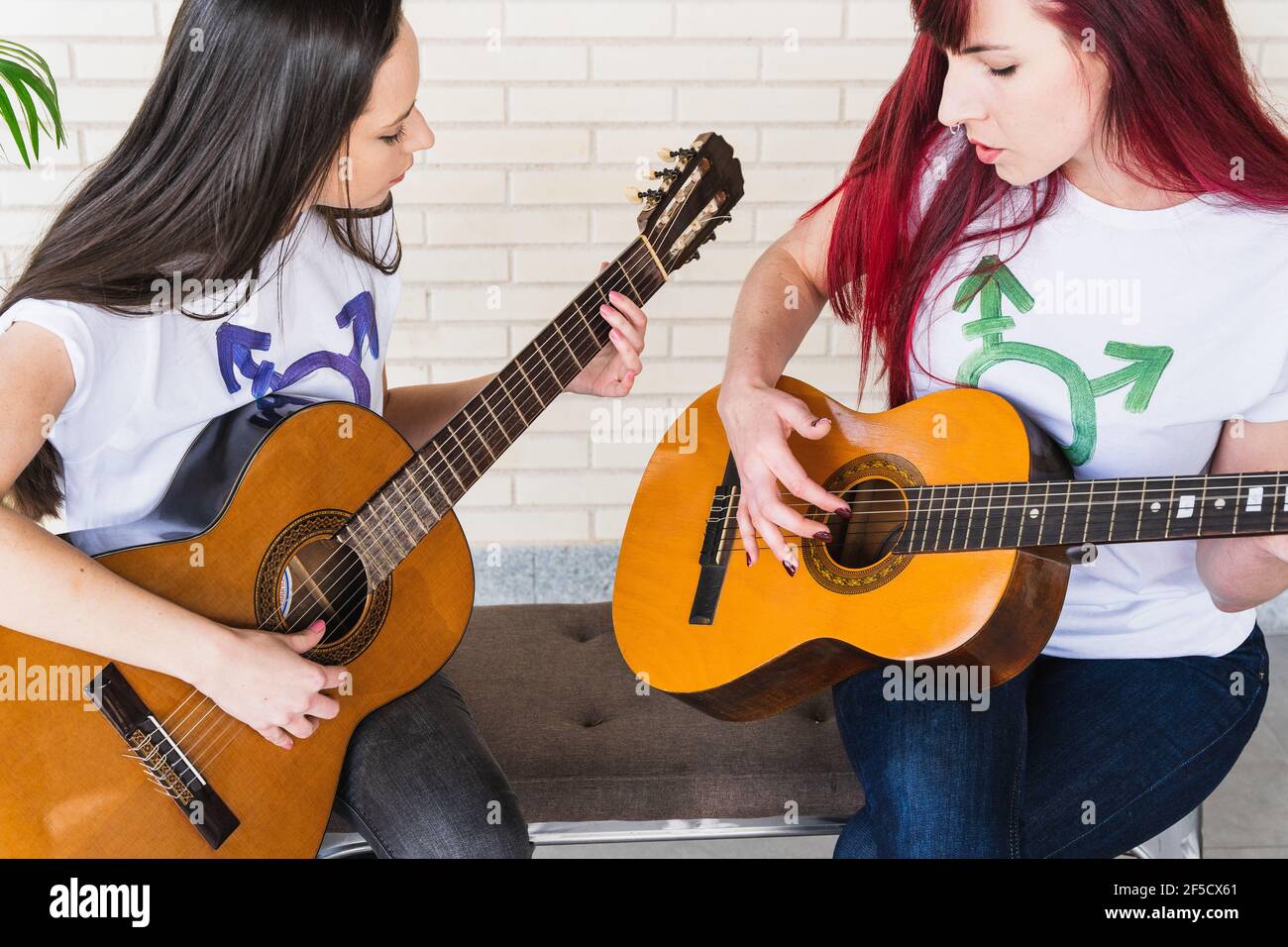 De dessus jeunes femmes guitaristes en t-shirts avec transgenre symbole jouant et chantant des chansons tout en étant assis sur le banc studio Banque D'Images