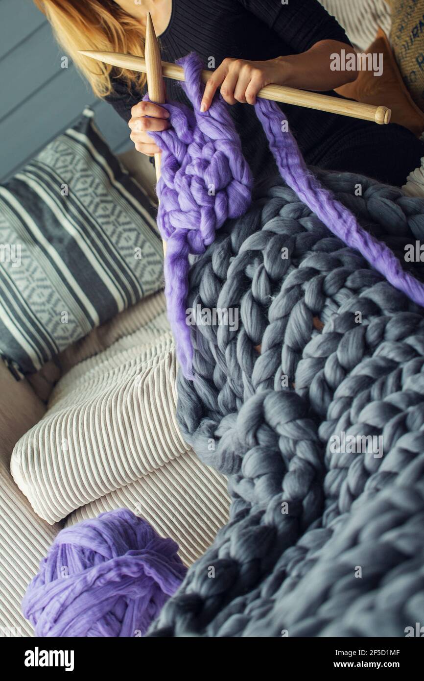 Une fille s'assoit sur un canapé à lait tisse un gris et couverture en  laine mérinos violette avec aiguilles à tricoter en bois Photo Stock - Alamy