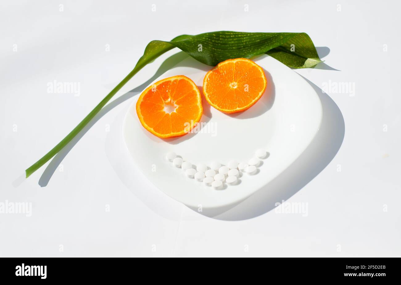 Les tranches d'orange sont deux yeux. Les pilules blanches sont la bouche. La feuille verte est le poil. La plaque est cette face. Thème alimentation saine et suppléments. Banque D'Images