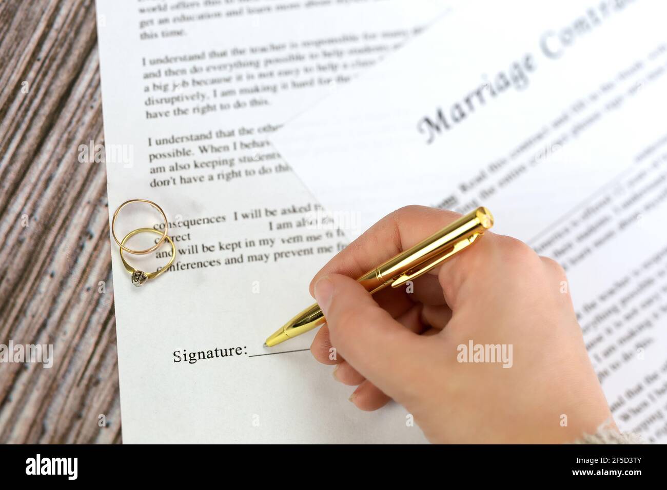 Contrat de mariage avec deux anneaux de mariage d'or et stylo d'or, accord prénuptial, macro gros plan, signer avec la signature, document, concept d'accord Banque D'Images