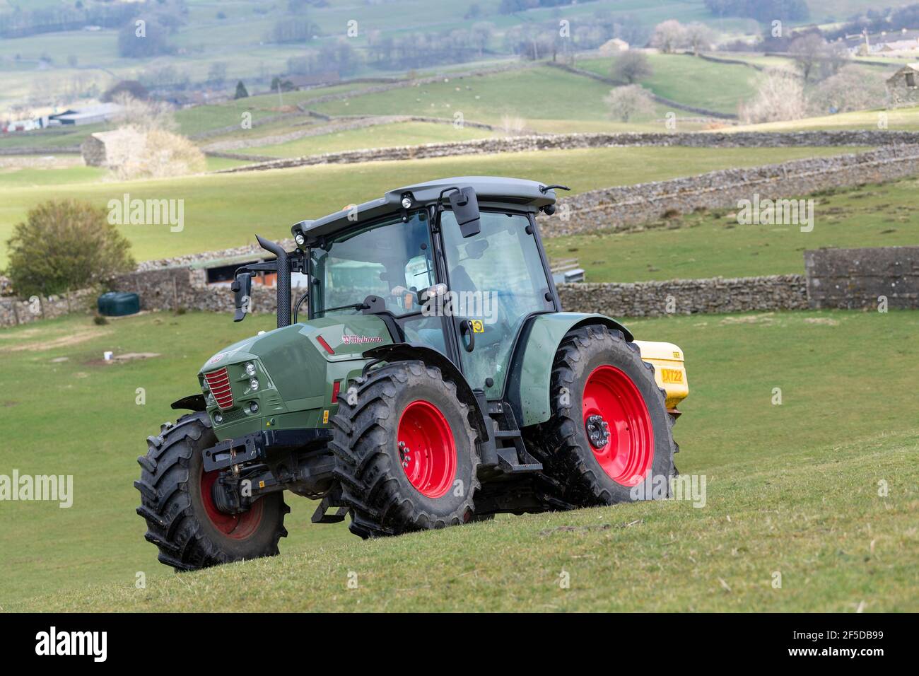 Agriculteur qui conduit un tracteur Hurlimann, étalant de l'engrais sur une prairie en montagne au printemps, dans le North Yorkshire, au Royaume-Uni. Banque D'Images