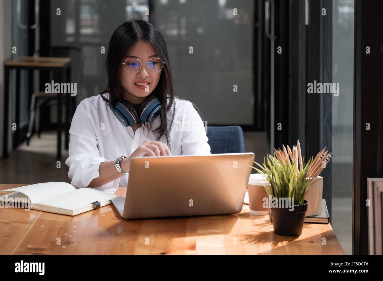 Fille asiatique avec des lunettes regarder l'ordinateur portable tout en faisant des devoirs faire des appels vidéo à l'étranger en utilisant la connexion d'amis d'Internet, formation en ligne Banque D'Images