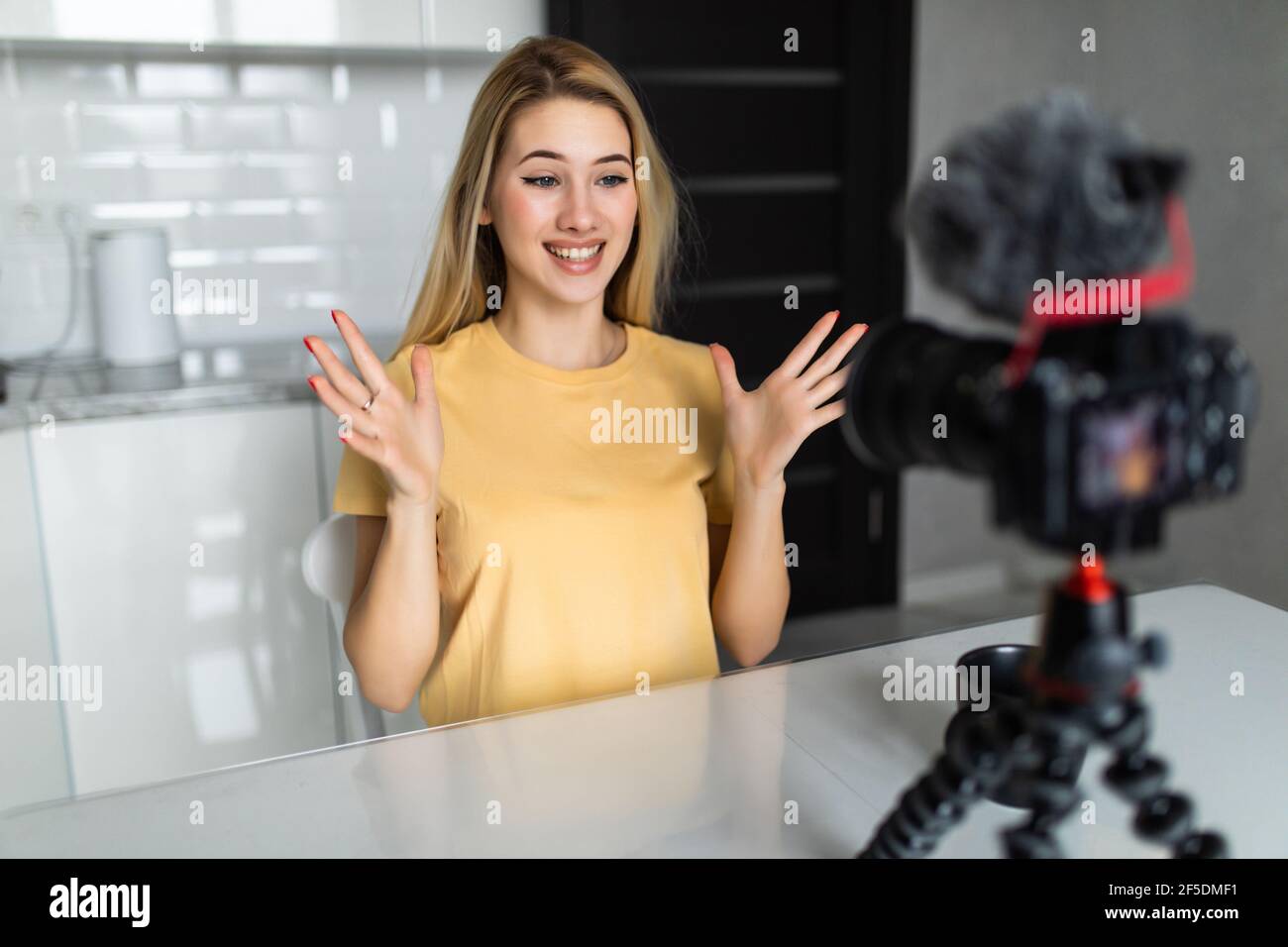 Femme attrayante enregistrant un blog vidéo sur un appareil photo reflex numérique dans la cuisine à la maison Banque D'Images