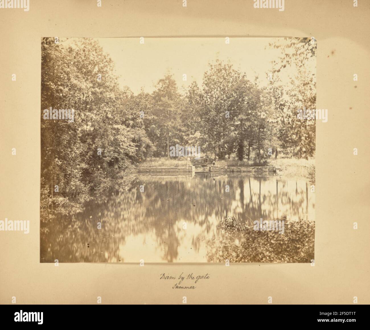 Barrage par la porte - été. Vue sur une rivière entourée d'une forêt. Un mur de support en pierre s'étend le long de l'extrémité pour créer un barrage avec un pont en bois. Deux personnes se tiennent sur le pont, et une troisième se trouve sur le mur avec les pieds nus qui pendent sur le bord. (Recto, montage) centre inférieur, écrit à la main à l'encre noire : « Dam by the gate / Summer » Banque D'Images