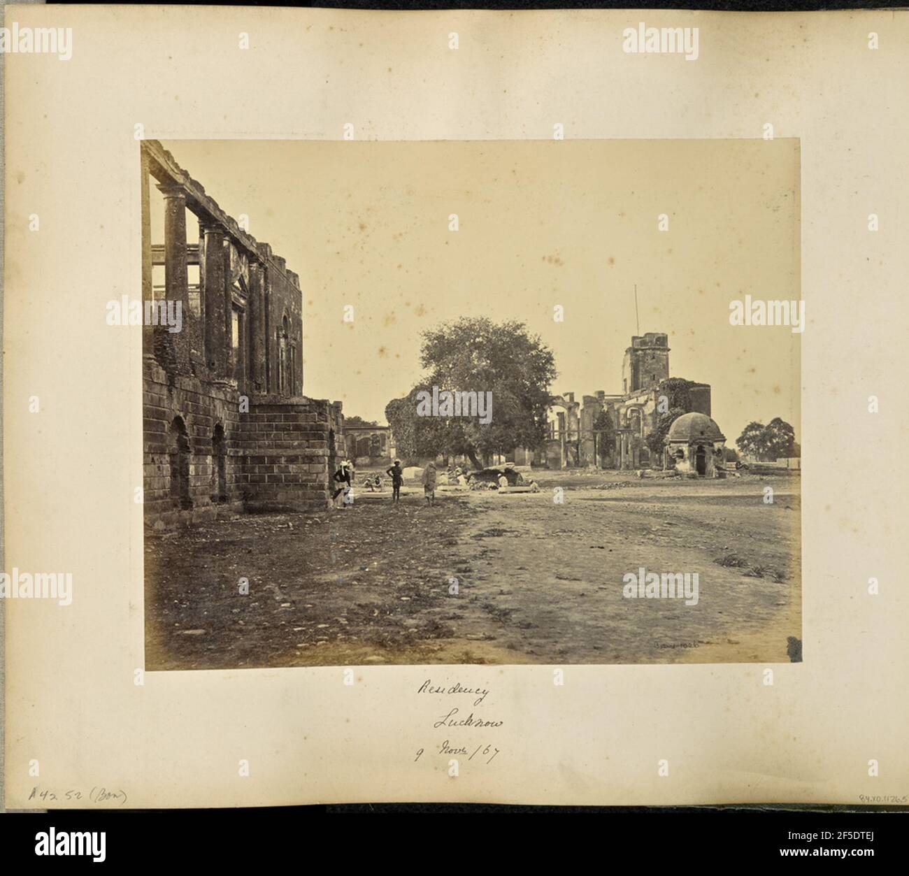 Lucknow; salle de résidence et de banquet. Vue sur les ruines de plusieurs bâtiments en pierre faisant partie de la résidence britannique. Un bâtiment sur le côté gauche de l'image comporte des colonnes rondes sans toit, et le bâtiment principal de la résidence se trouve sur la droite, avec une tour et un mât de pavillon. Plusieurs hommes peuvent être vus près d'un arbre entre les deux bâtiments. (Recto, image) en bas à droite, manuscrit en négatif: '1026' (Recto, Mount) en bas à gauche, manuscrit en crayon: 'A42.52 (Bou)' en bas au centre, manuscrit en encre noire: 'Résidence / Lucknow / 9 Novr /67' Banque D'Images