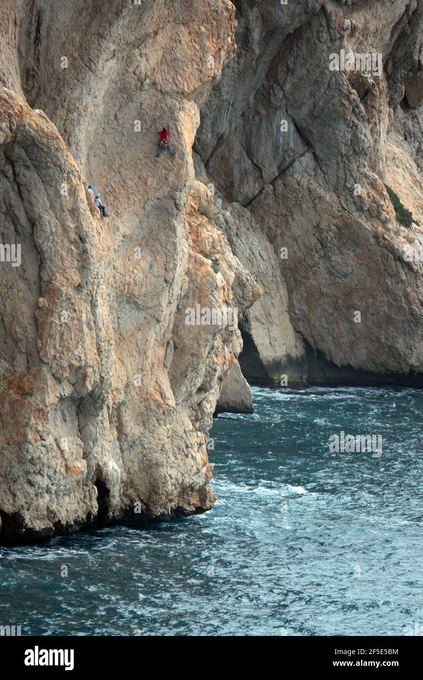 De minuscules grimpeurs de rochers sur les immenses falaises rouges de Toix à Calpe, Costa Blanca, Espagne Banque D'Images