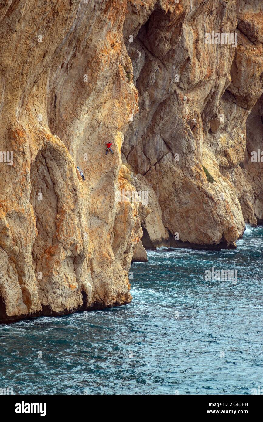 De minuscules grimpeurs de rochers sur les immenses falaises rouges de Toix à Calpe, Costa Blanca, Espagne Banque D'Images