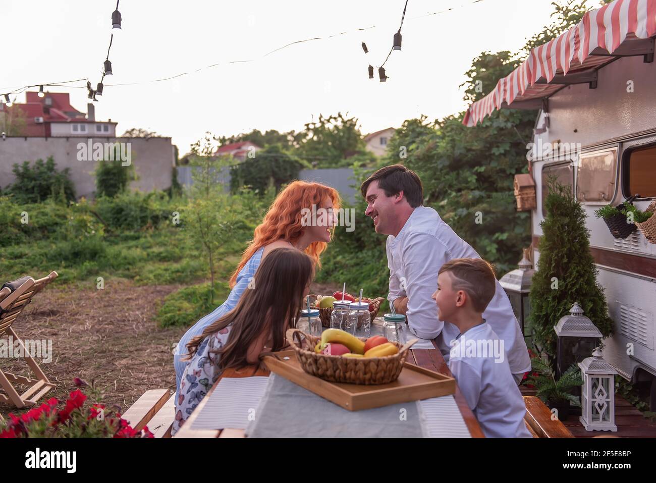 Une famille heureuse s'assoit à une table en bois, boit la limonade ensemble par un camion-remorque. Pique-nique, camping de fin de semaine avec les enfants. Voyagez dans un camping-auto. PAREN Banque D'Images