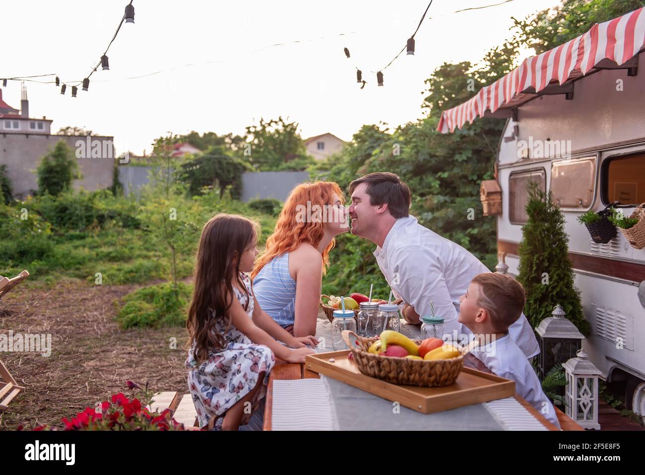 Une famille heureuse s'assoit à une table en bois, boit la limonade ensemble par un camion-remorque. Pique-nique, camping de fin de semaine avec les enfants. Voyagez dans un camping-auto. PAREN Banque D'Images