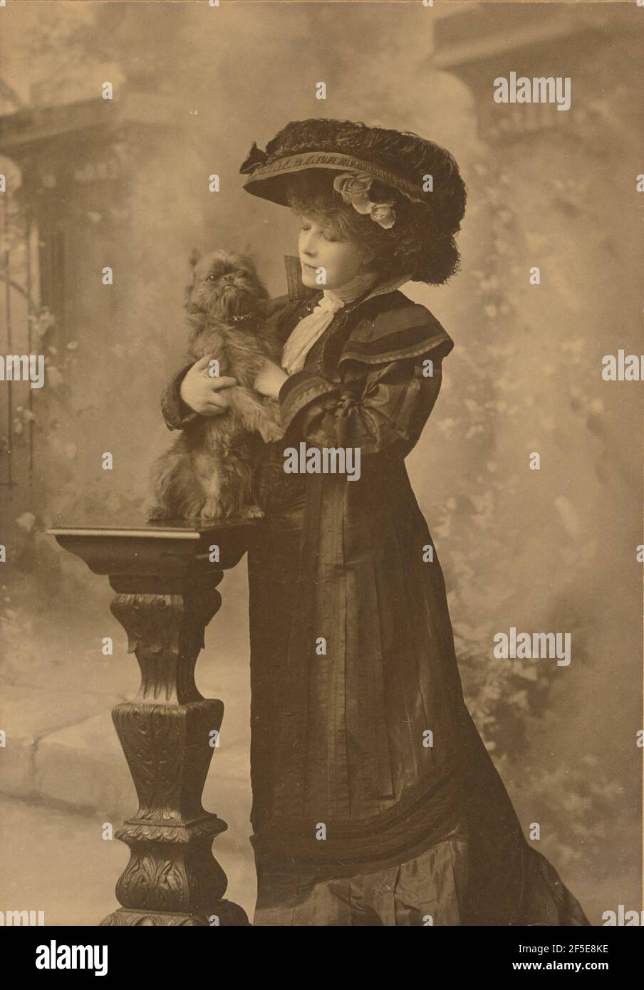 Sarah Bernhardt debout dans un cadre studio, tenant un petit chien noir sur un piédestal en bois sculpté et orné. Theodore C. Marceau (cuisine américaine, 1859 - 1922) Banque D'Images