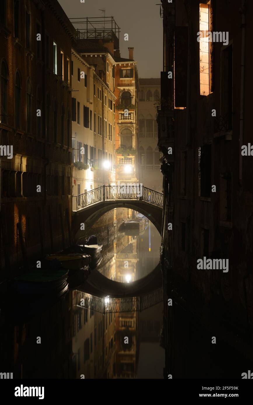 Vue de nuit sur le canal à Venise avec pont lumineux, maisons et bateaux, Italie Banque D'Images