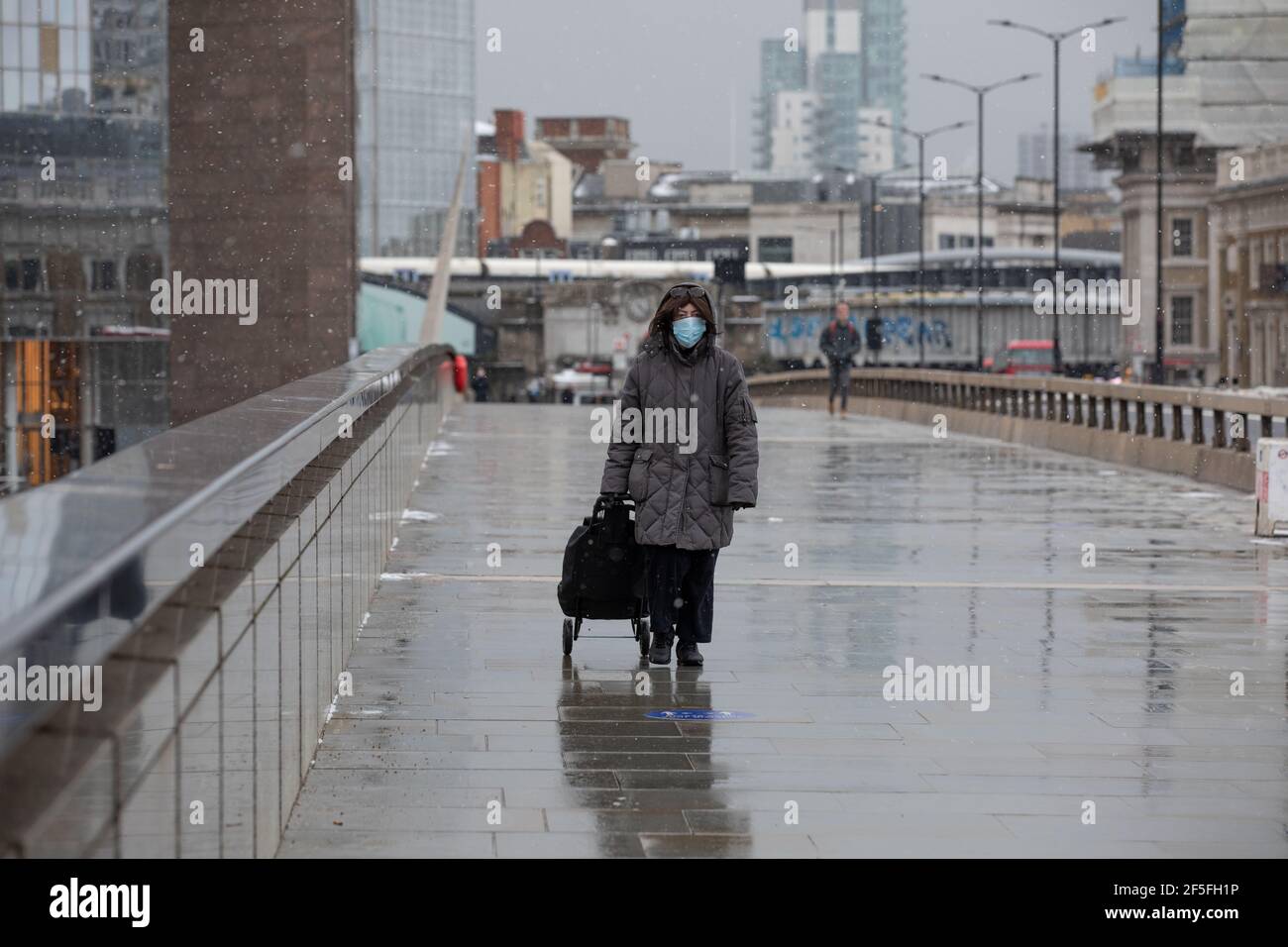 Une femme portant un masque de visage marche seule à travers le London Bridge lors d'une matinée hivernale froide à l'ouest Banque D'Images