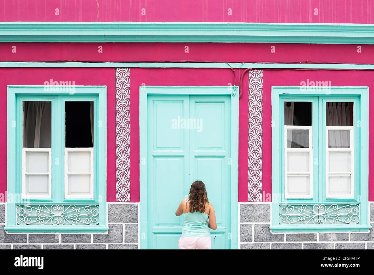 Fille devant la façade d'une maison colorée en fuchsia et eau verte Banque D'Images