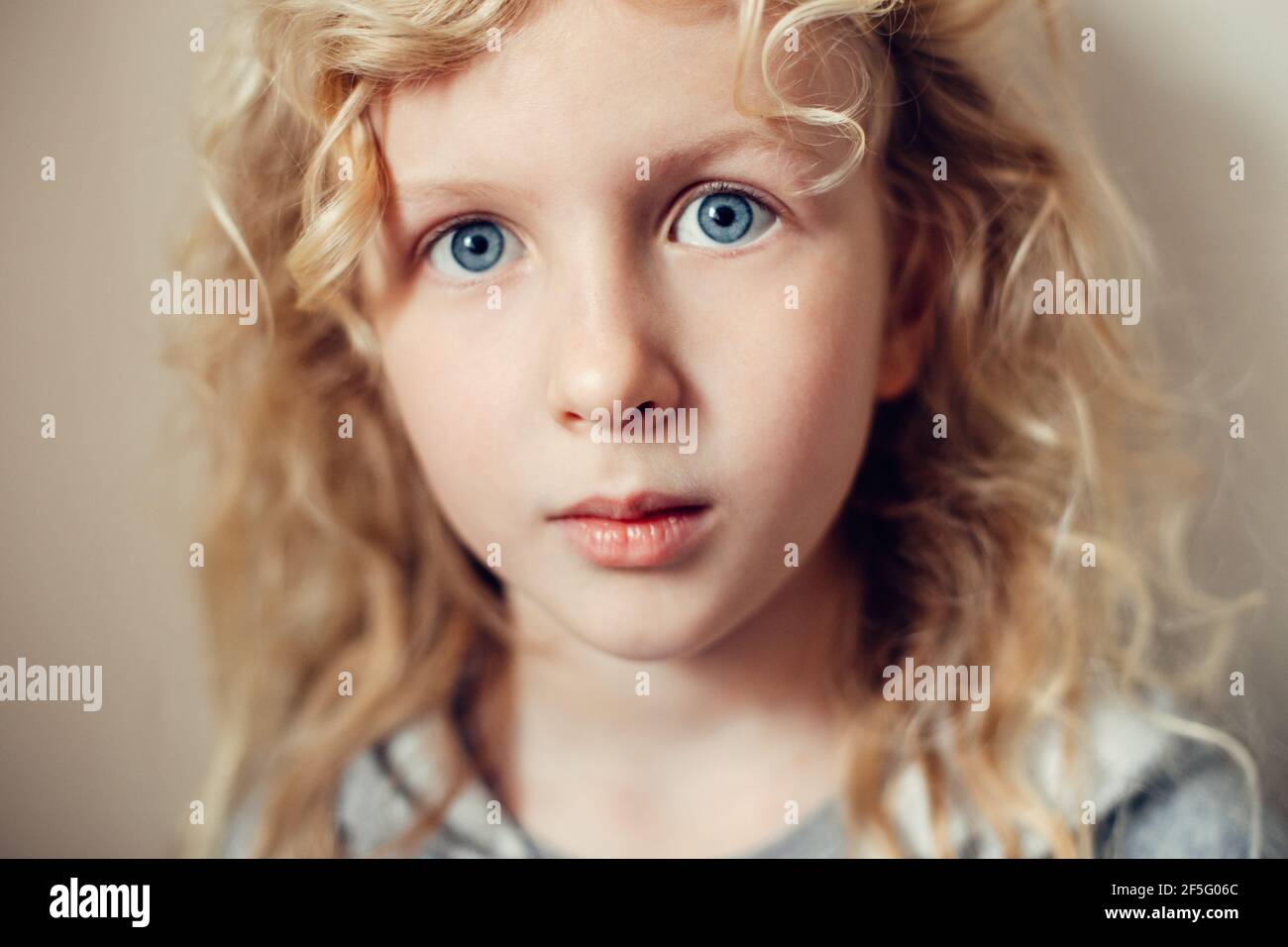 Gros plan portrait de la belle pensive sérieuse caucasienne blonde fille avec de longs cheveux sur fond beige clair neutre. Jolie fille vraie enfant avec natu Banque D'Images