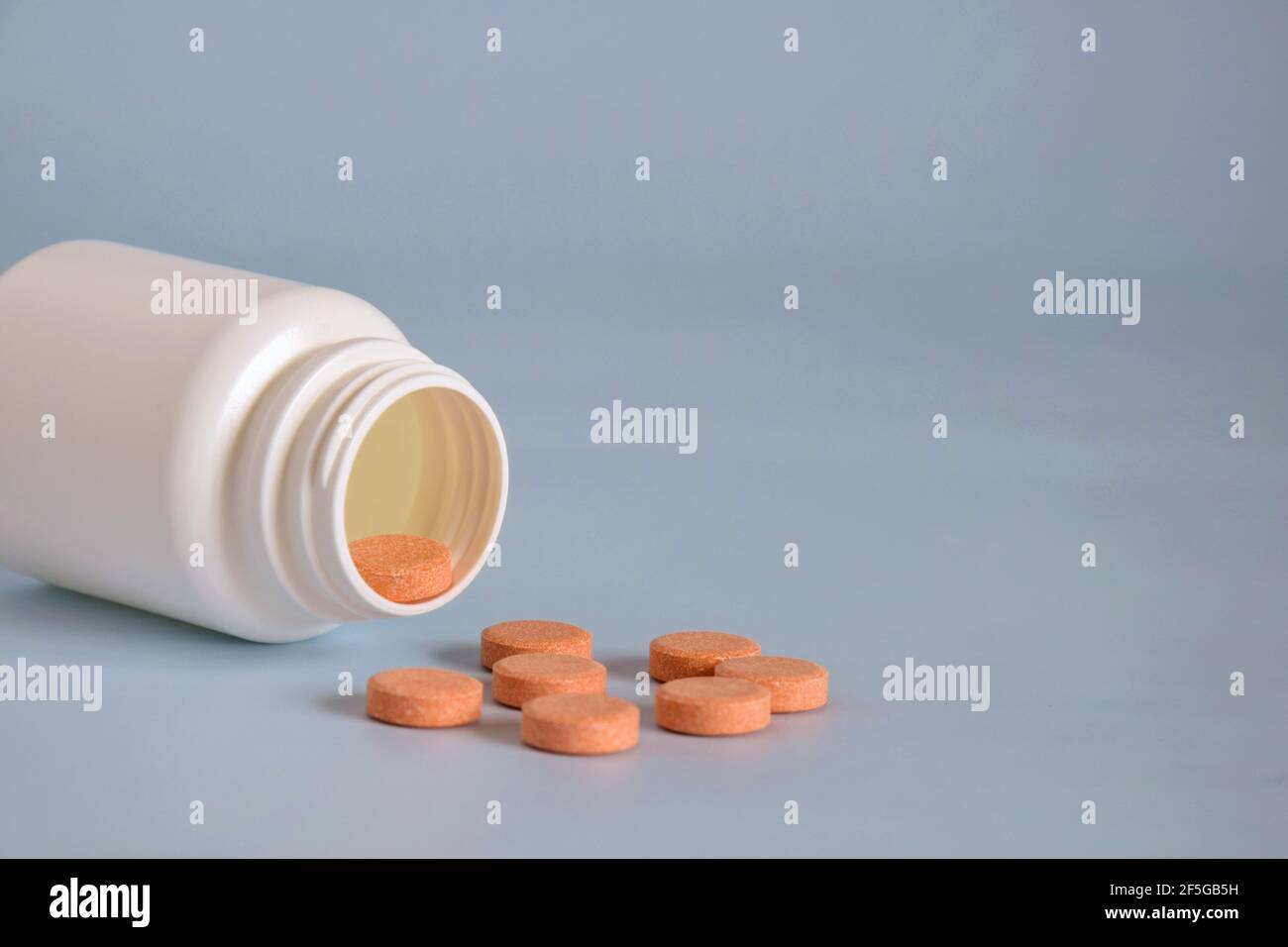 Pilules de médecine d'orange naturelle dans un pot ouvert en plastique retourné sur le devant de la table. Médecine concept des médicaments, des comprimés, des médicaments et des pilules sur fond gris. Banque D'Images
