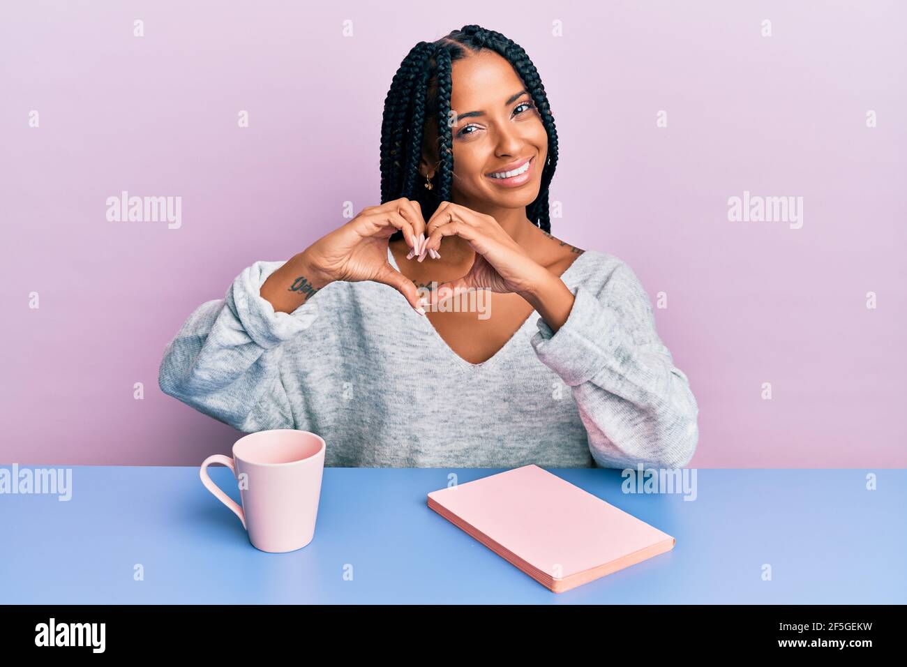 Belle femme hispanique lisant un livre et buvant un café souriant dans l'amour montrant le symbole du coeur et la forme avec les mains. Concept romantique. Banque D'Images