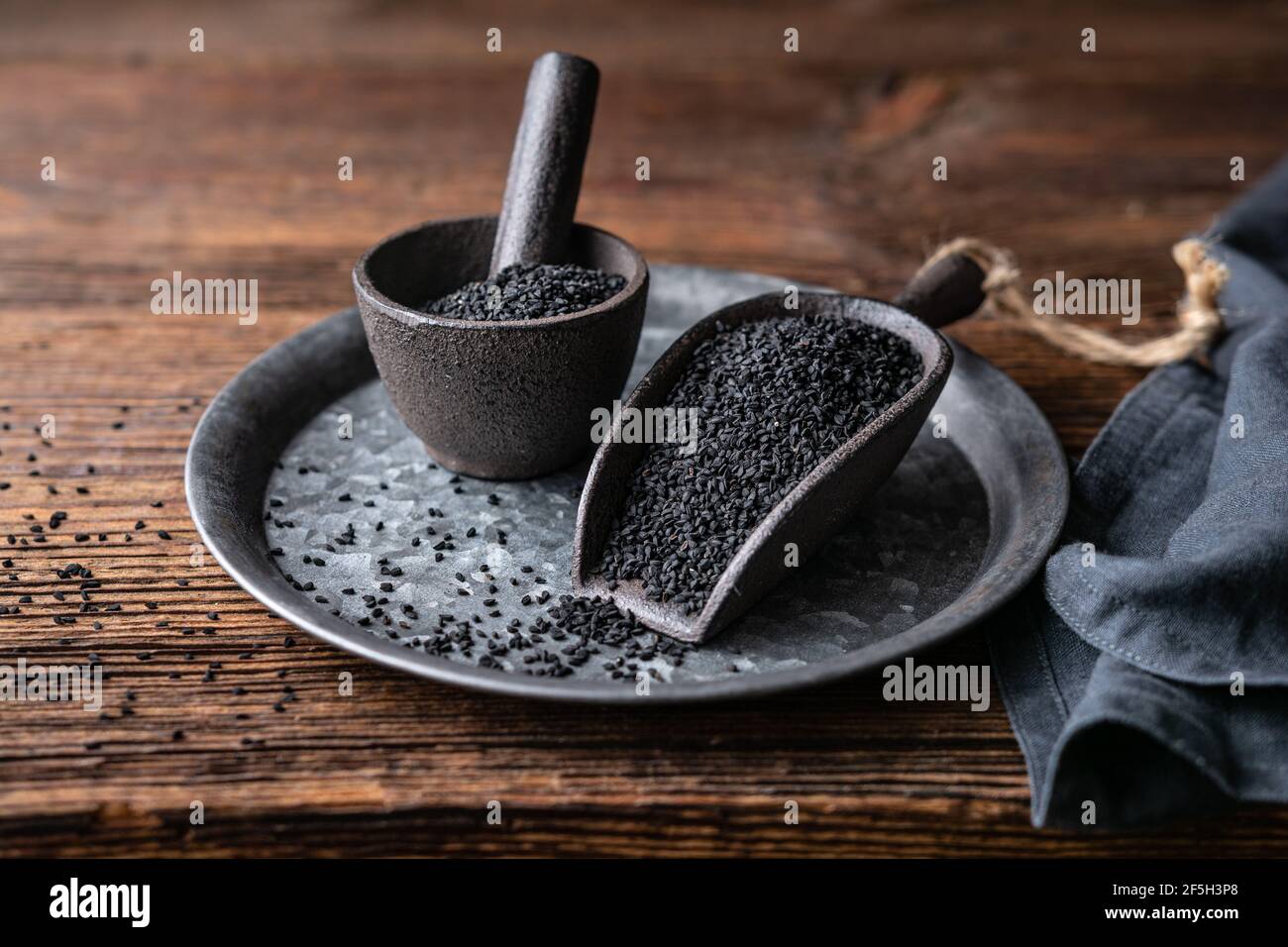 Graines de Nigella sativa également connu sous le nom de cumin noir, kalo jeera, kalonji et carvi noir dans la pelle en fer et le mortier sur fond rustique en bois Banque D'Images