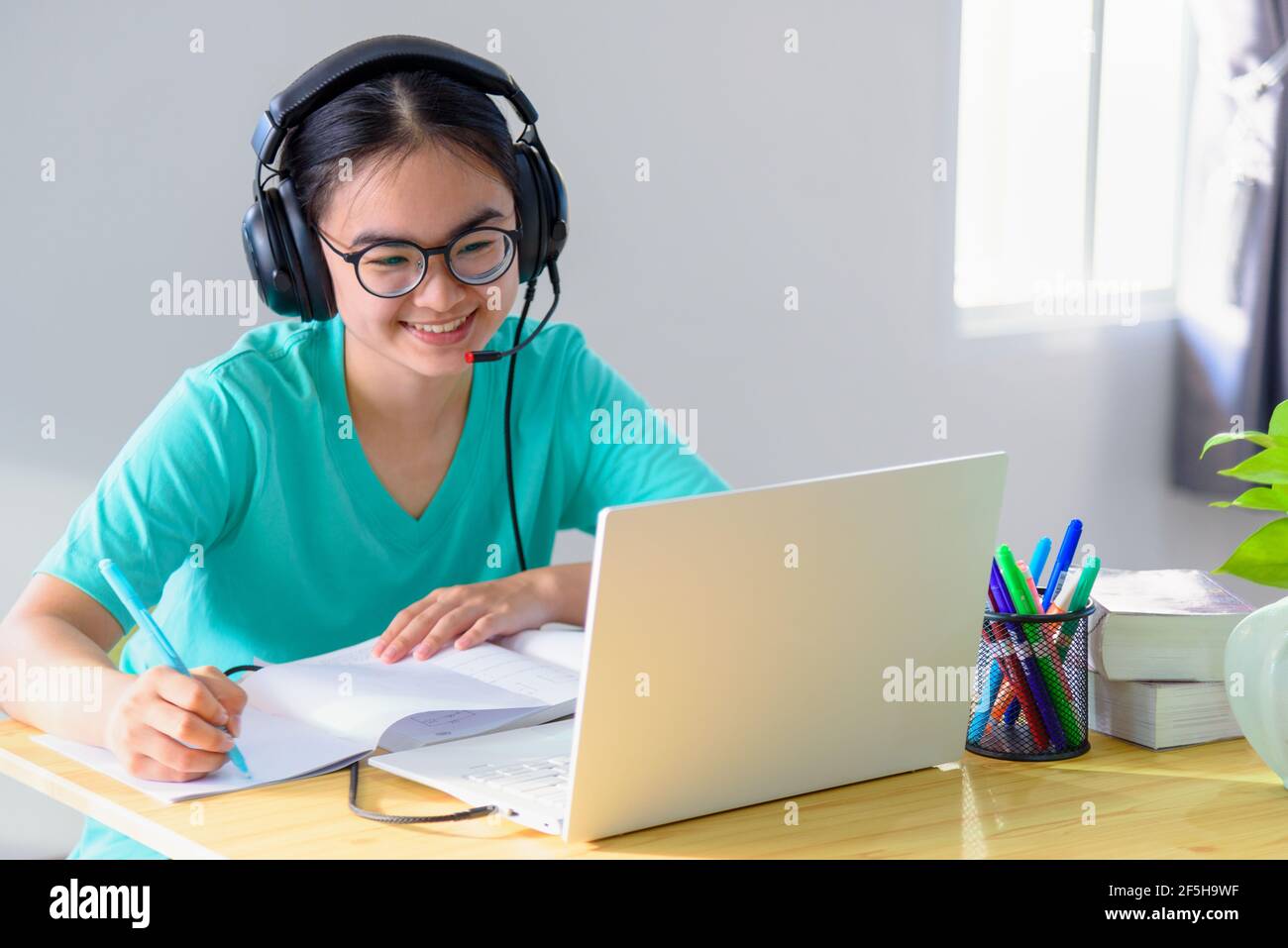 Asiatique jeune femme étudiant avec des lunettes casque fille étude heureux écrire une note sur un livre regardant la vidéo conférence ordinateur portable cours universitaire sur Banque D'Images