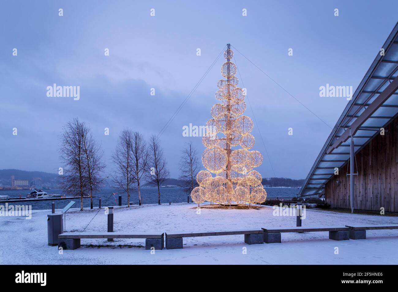 Décoration de Noël dans l'espace public à Oslo, Norvège sur la froide soirée d'hiver. Un arbre de Noël moderne illumine la soirée bleue autour d'un front de mer enneigé Banque D'Images