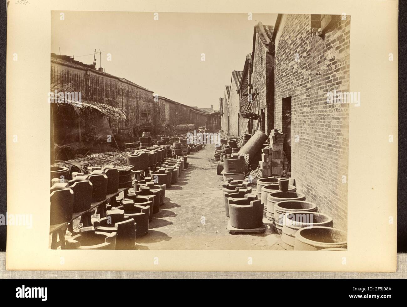 Vue sur une allée bordée de bâtiments en briques et de conteneurs au sol. Lai, Afong (chinois, vers 1839 - 1890) Banque D'Images