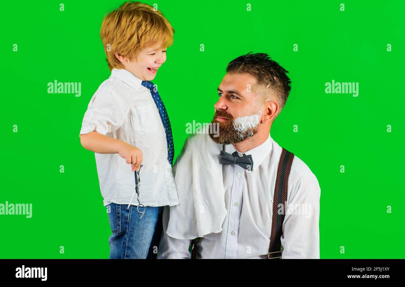 Fête des pères. Fils et papa dans un salon de coiffure. Rasage de la barbe en barbershop. Assistant pour papa. Salon pour hommes. Banque D'Images