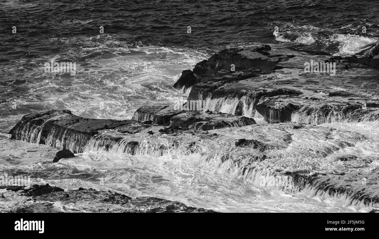 les vagues déferlent de la roche volcanique noire plate sur un orage jour Banque D'Images