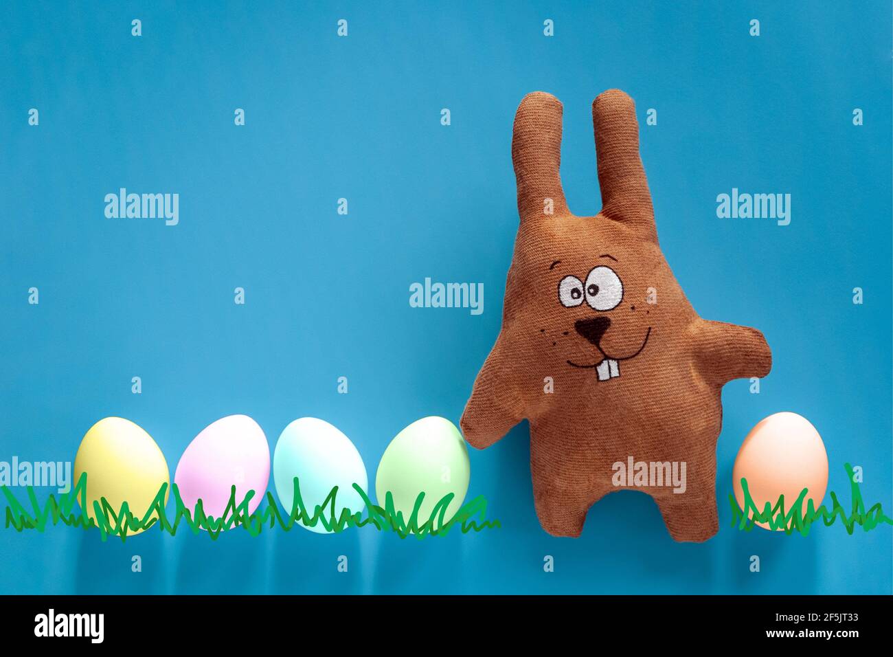 Chasse de Pâques avec lapin jouet et œufs de couleur dans le verre sur fond bleu Banque D'Images