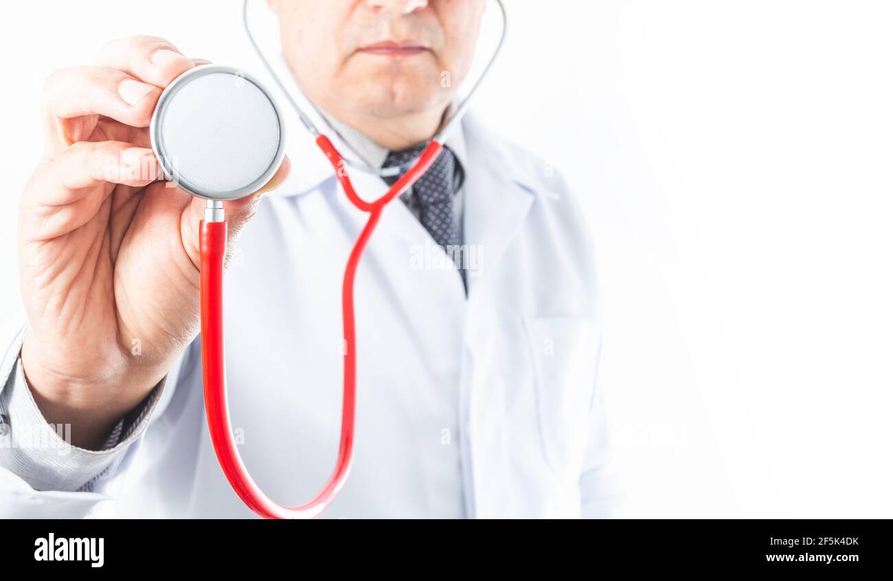 Mise au point sélective d'une main tenant un stéthoscope rouge, avec un médecin dans un manteau blanc et l'attache hors de la mise au point sur fond blanc. Bon espace de copie Banque D'Images