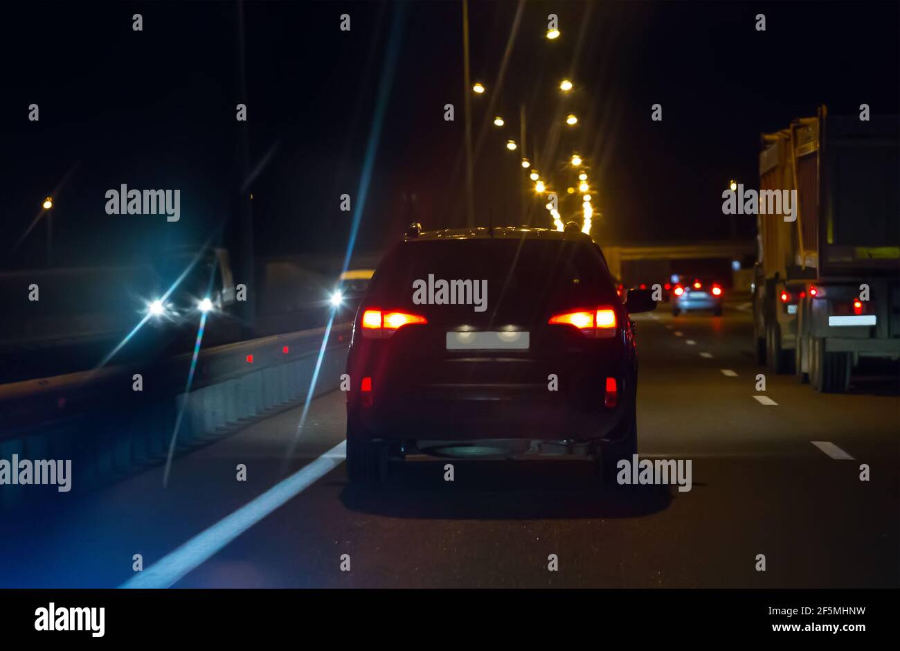 Les voitures avec feux allumés se déplacent de nuit sur de larges routes à plusieurs voies. Vue arrière. Banque D'Images