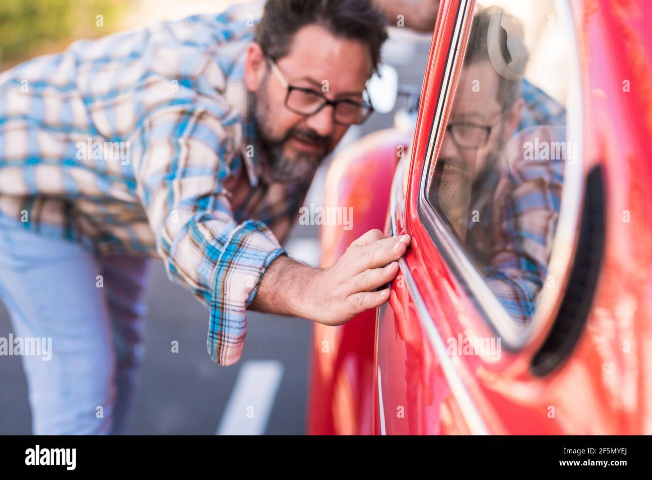 L'homme de taille basse barbu adulte vérifie le vernis de son beau voiture extérieure - les gens et le transport automobile amour et soin concept - le conducteur regarde Banque D'Images