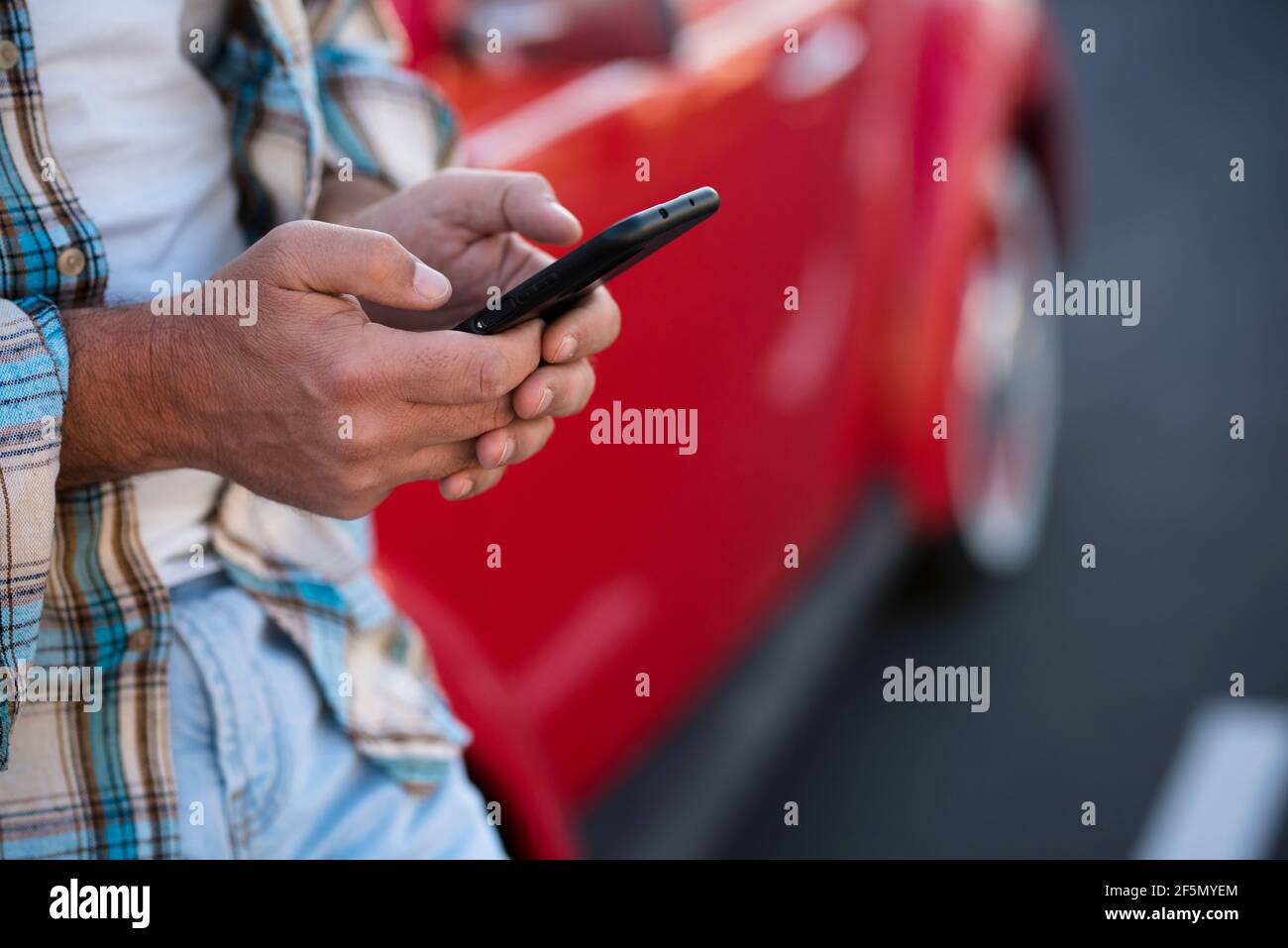 Gros plan sur un homme utilisant un téléphone à l'extérieur - personnes méconnaissables avec un smartphone cellulaire pour discuter ou envoyer des sms avec la voiture en arrière-plan - style de vie moderne avec Banque D'Images
