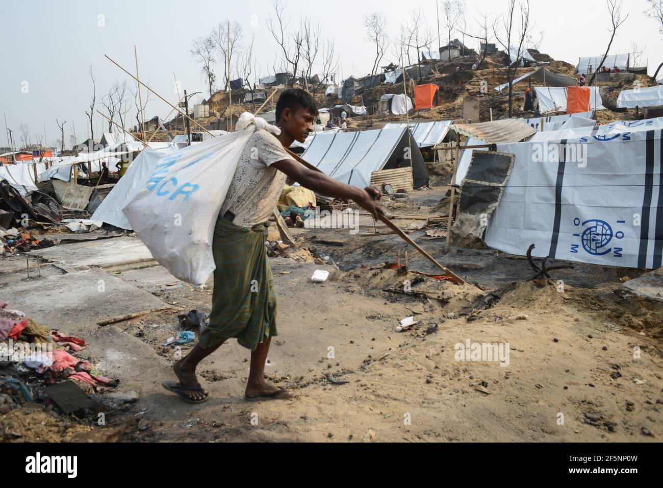 Un homme porte des restes charrés de ses effets à un Site d'abris temporaires mis en place pour les réfugiés déplacés de Rohingya jours après un incendie à un réfugié Banque D'Images