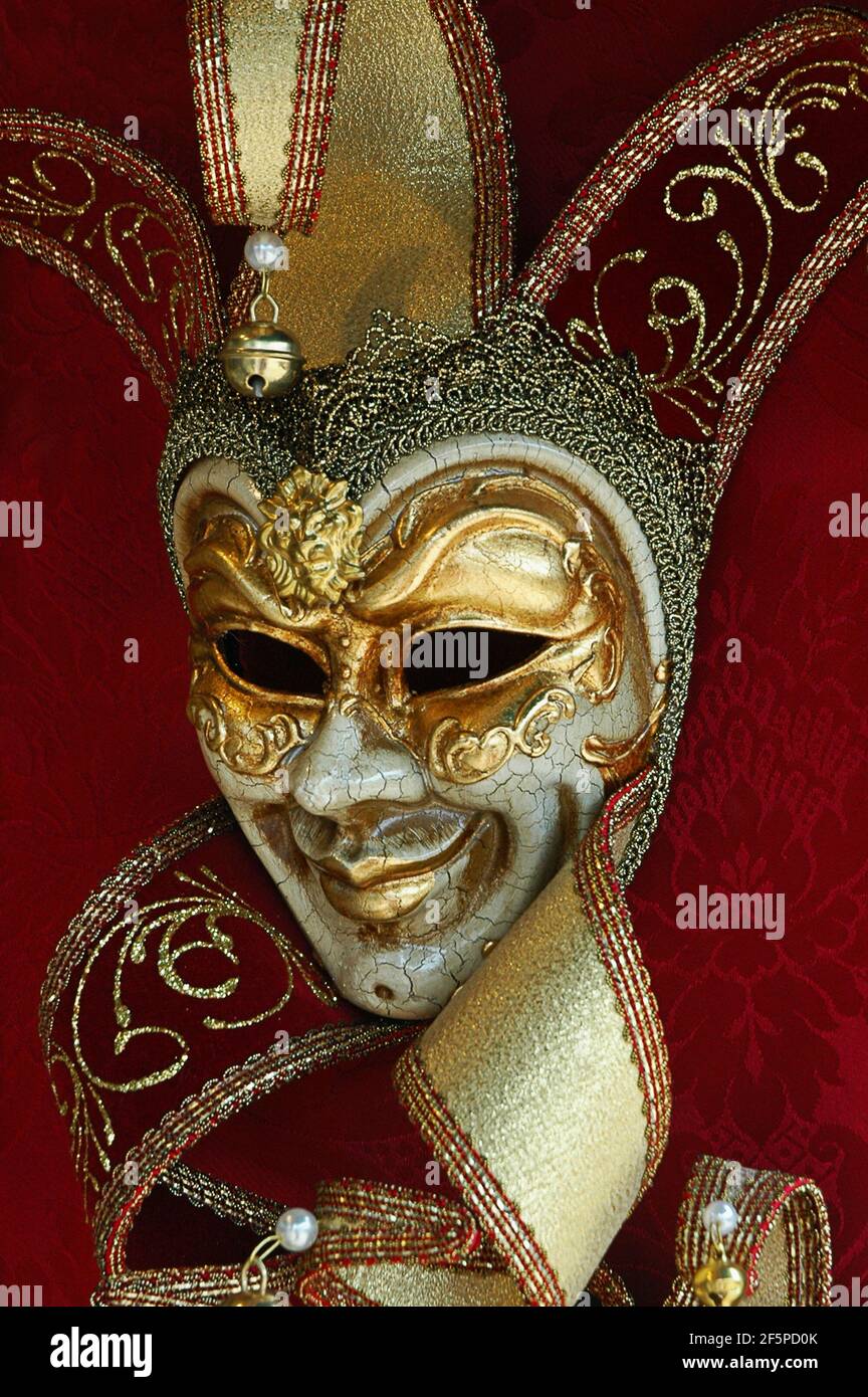 Un masque de carnaval vénitien typique représentant Arlecchino conçu dans le traditionnel style avec feuille d'or et finition de peinture craquelée sur un arrière-plan rouge Banque D'Images