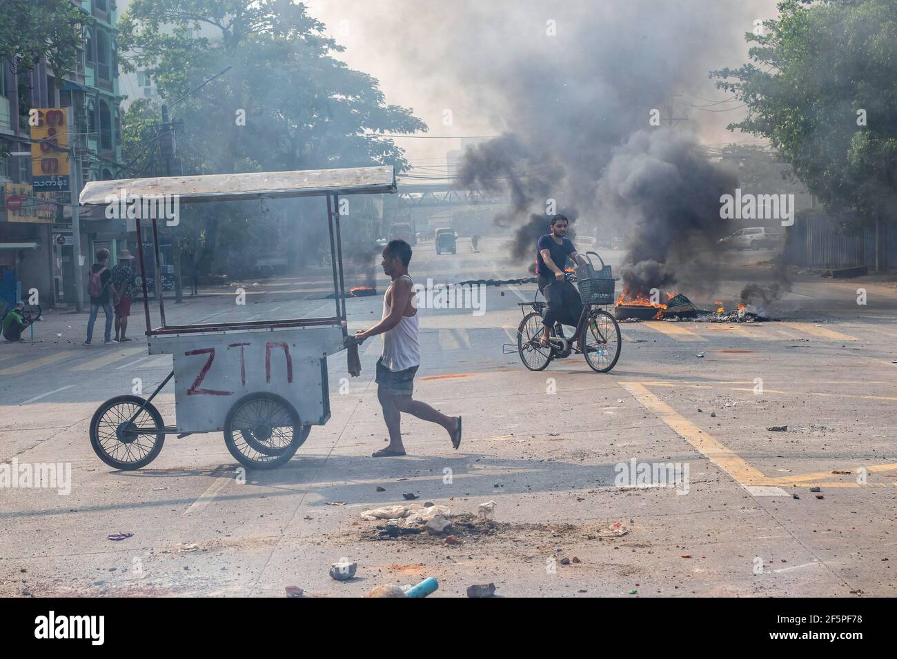 Un cycliste passe devant des pneus en feu dans la rue lors d'une manifestation contre le coup d'État militaire.la police et les militaires du Myanmar (tatmadow) ont attaqué les manifestants avec des balles en caoutchouc, des munitions réelles, des gaz lacrymogènes et des bombes lacrymogènes en réponse aux manifestants anti-coup d'État militaire de samedi, tuant plus de 90 personnes et en blessant beaucoup d'autres. Au moins 300 personnes ont été tuées au Myanmar depuis le coup d'État du 1er février, a déclaré un responsable des droits de l'homme de l'ONU. L'armée du Myanmar a détenu le conseiller d'État du Myanmar Aung San Suu Kyi le 01 février 2021 et a déclaré l'état d'urgence tout en prenant le pouvoir Banque D'Images