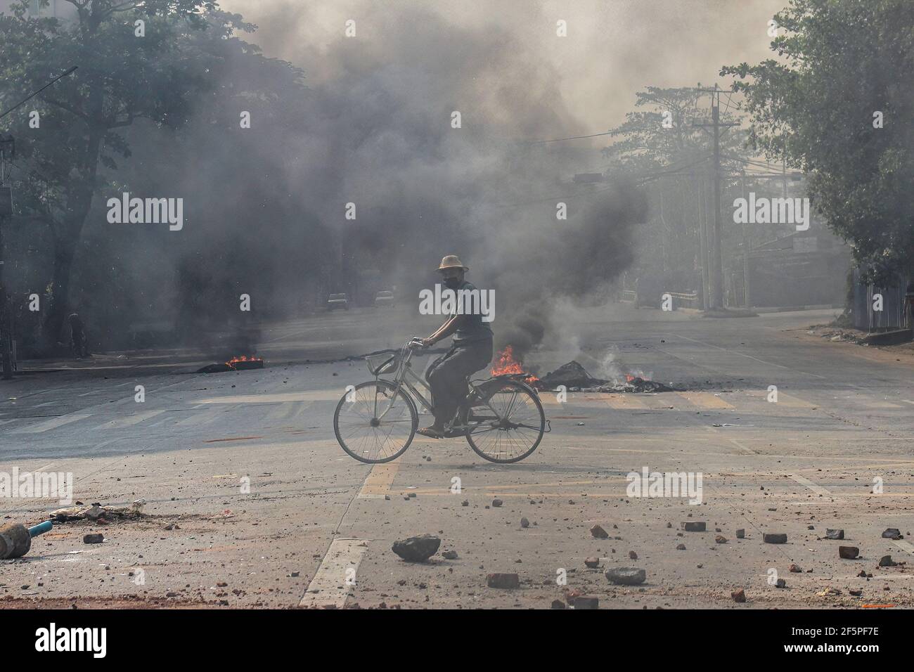 Un cycliste passe devant des pneus en feu dans la rue lors d'une manifestation contre le coup d'État militaire.la police et les militaires du Myanmar (tatmadow) ont attaqué les manifestants avec des balles en caoutchouc, des munitions réelles, des gaz lacrymogènes et des bombes lacrymogènes en réponse aux manifestants anti-coup d'État militaire de samedi, tuant plus de 90 personnes et en blessant beaucoup d'autres. Au moins 300 personnes ont été tuées au Myanmar depuis le coup d'État du 1er février, a déclaré un responsable des droits de l'homme de l'ONU. L'armée du Myanmar a détenu le conseiller d'État du Myanmar Aung San Suu Kyi le 01 février 2021 et a déclaré l'état d'urgence tout en prenant le pouvoir Banque D'Images