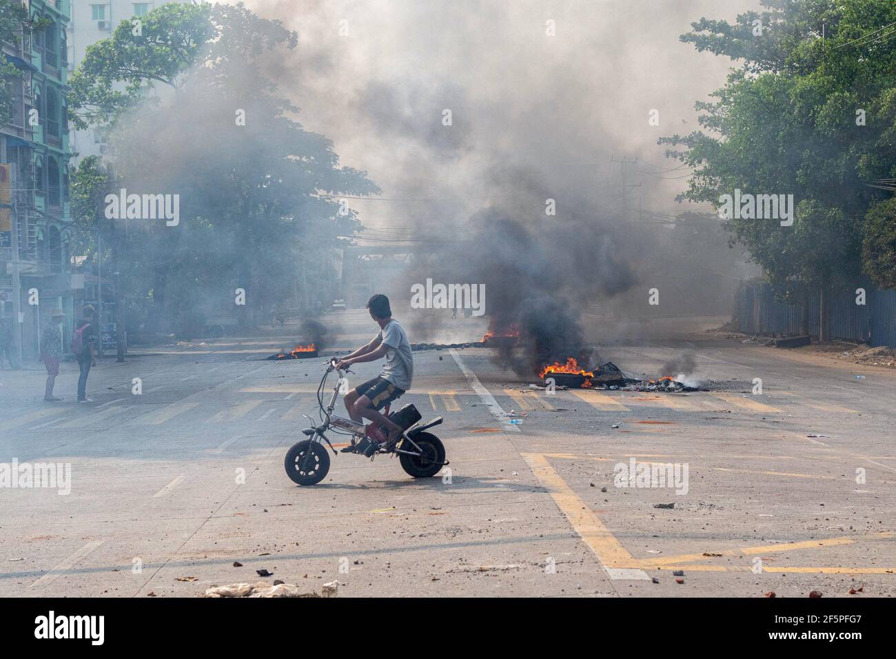 Un automobiliste passe devant des pneus en feu dans la rue lors d'une manifestation contre le coup d'État militaire.la police et les militaires du Myanmar (tatmadow) ont attaqué les manifestants avec des balles en caoutchouc, des munitions vivantes, des gaz lacrymogènes et des bombes lacrymogènes en réponse aux manifestants anti-coup d'État militaire de samedi, tuant plus de 90 personnes et en blessant beaucoup d'autres. Au moins 300 personnes ont été tuées au Myanmar depuis le coup d'État du 1er février, a déclaré un responsable des droits de l'homme de l'ONU. L'armée du Myanmar a détenu le conseiller d'État du Myanmar Aung San Suu Kyi le 01 février 2021 et a déclaré l'état d'urgence en s'emparant de la puissance Banque D'Images
