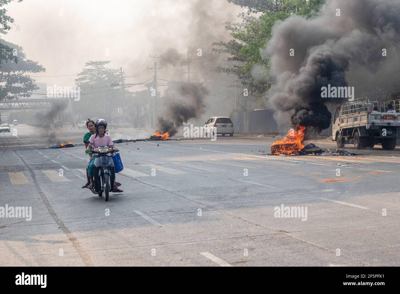 Un automobiliste passe devant des pneus en feu dans la rue lors d'une manifestation contre le coup d'État militaire.la police et les militaires du Myanmar (tatmadow) ont attaqué les manifestants avec des balles en caoutchouc, des munitions vivantes, des gaz lacrymogènes et des bombes lacrymogènes en réponse aux manifestants anti-coup d'État militaire de samedi, tuant plus de 90 personnes et en blessant beaucoup d'autres. Au moins 300 personnes ont été tuées au Myanmar depuis le coup d'État du 1er février, a déclaré un responsable des droits de l'homme de l'ONU. L'armée du Myanmar a détenu le conseiller d'État du Myanmar Aung San Suu Kyi le 01 février 2021 et a déclaré l'état d'urgence en s'emparant de la puissance Banque D'Images