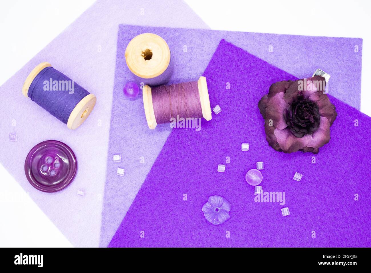 Articles de couture pourpres : feutre dans trois nuances de lilas, bobines en bois avec fil, perles, boutons, et une rose pourpre. Banque D'Images