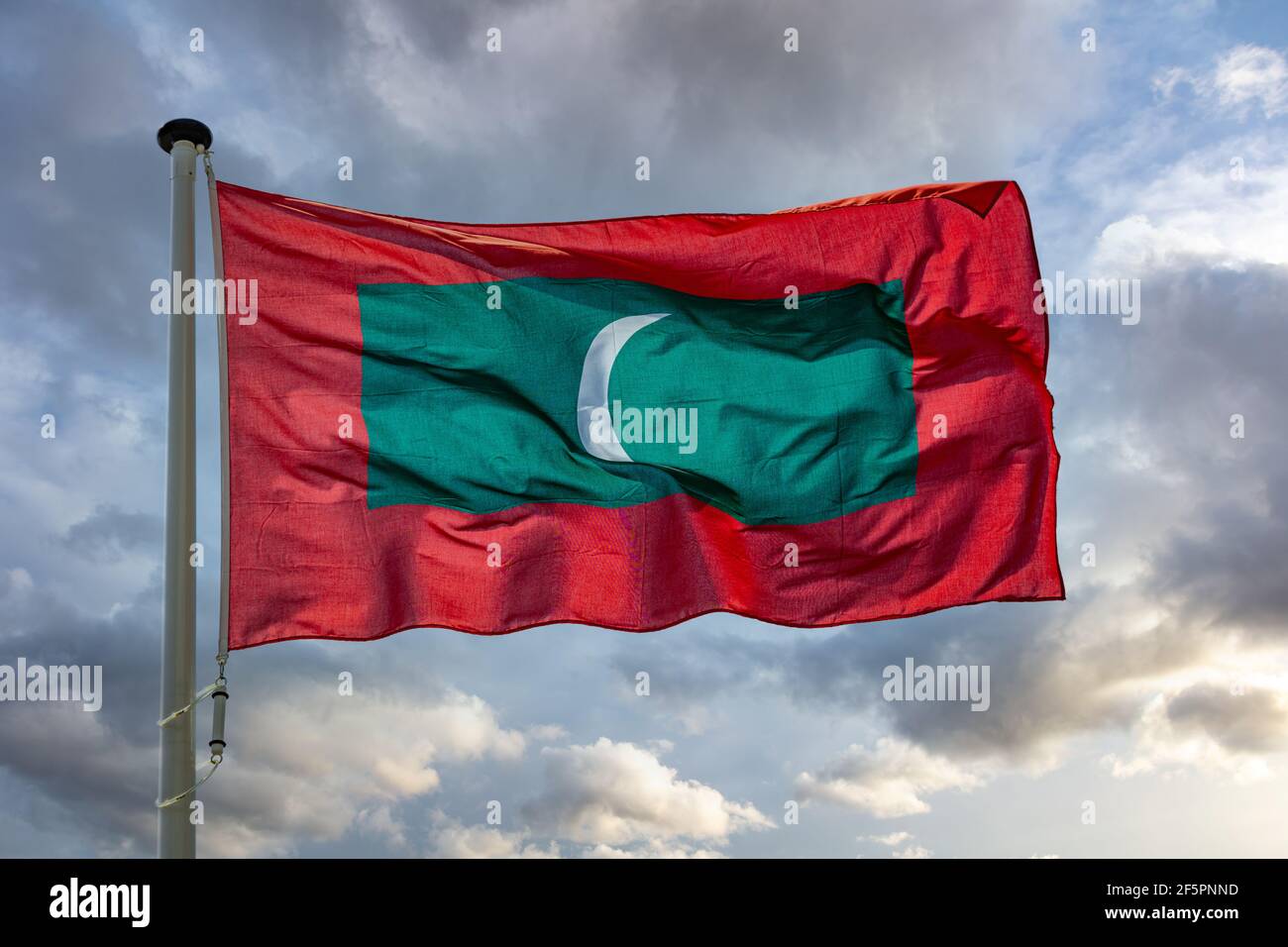 Symbole Maldives. Drapeau national de la République des Maldives sur un poteau agitant contre fond ciel nuageux. Banque D'Images