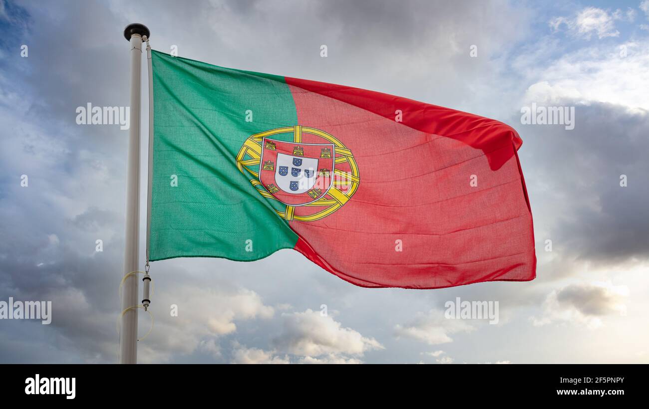 Symbole du Portugal. Drapeau national de la République portugaise sur un poteau agitant sur fond ciel nuageux. Banque D'Images