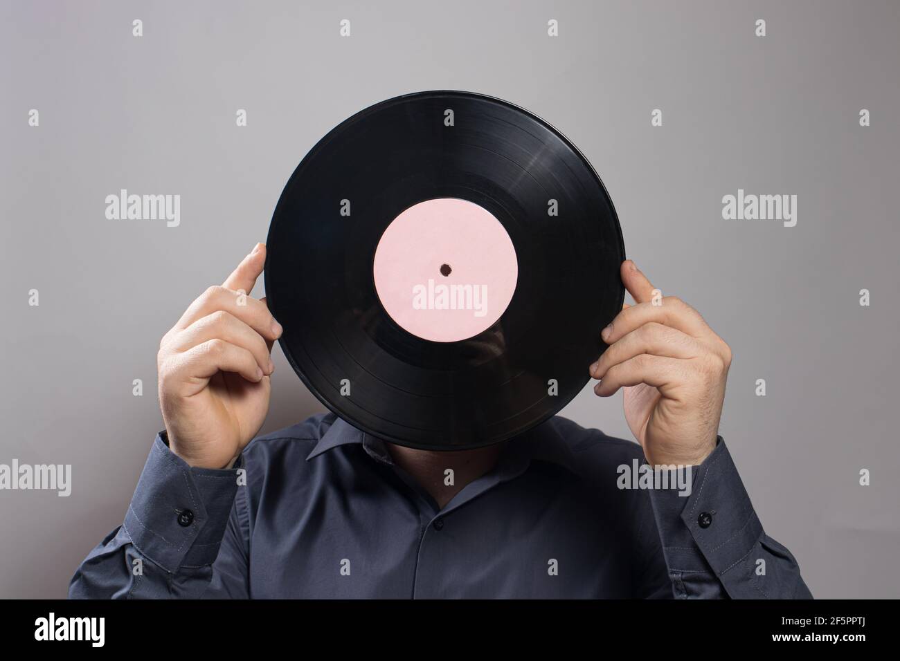 Un homme dans une chemise tient un vieux disque de vinyle vintage au lieu de sa tête. L'idée d'un amour des antiquités. Banque D'Images