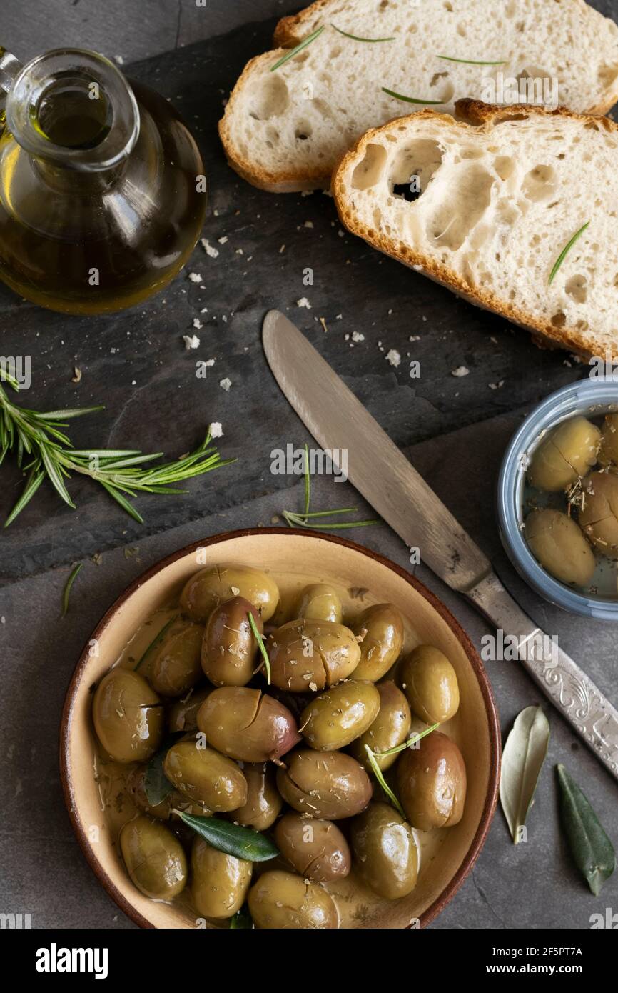 Pain de ciabatta en tranches italiennes sur planche à découper avec herbes, huile extra vierge et olives marinées sur fond de grunge foncé Banque D'Images